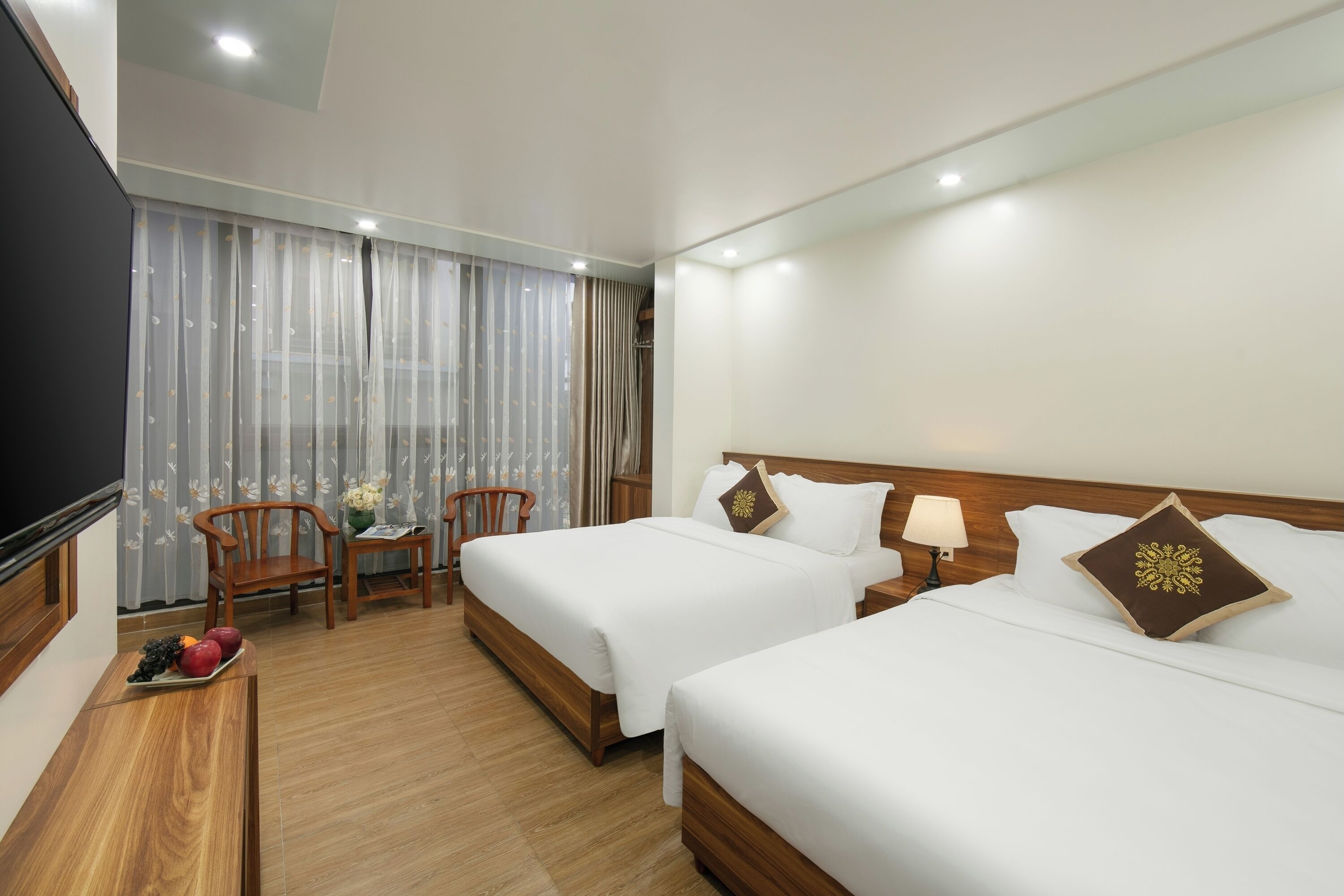 A hotel room with two beds, a TV, a desk with fruit, and a chair.