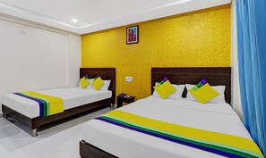 A hotel room with two beds, a yellow textured wall, and a framed picture above the beds. - Itsy Hotels Harsha Comforts, 600 Mts From Coffee Museum (Chikkamagaluru)