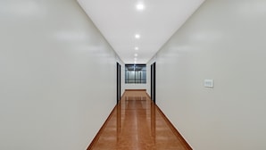 Um corredor comprido e estreito com paredes brancas e chão de azulejos marrons.