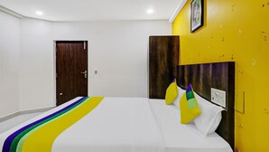 Quarto de hotel com cama, porta de madeira, parede amarela e quadro emoldurado.