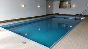 En inomhuspool med kristallklart blått vatten, kaklade väggar och ett kaklat golv.