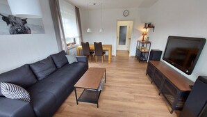 Ett modernt vardagsrum med en svart soffa, ett träbord och en tv som står på ett träställ.