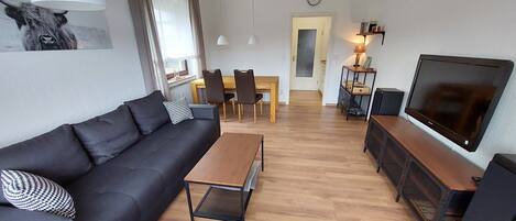A modern living room with a black sofa, wooden coffee table, and a TV on a wooden stand.