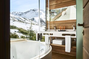 A bathroom with a bathtub, wooden vanity, and a view of snow-covered mountains.