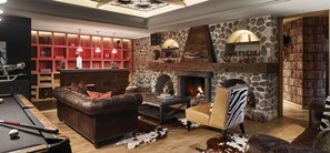 A cozy living room with a fireplace, a pool table, leather sofas, and a bookshelf.