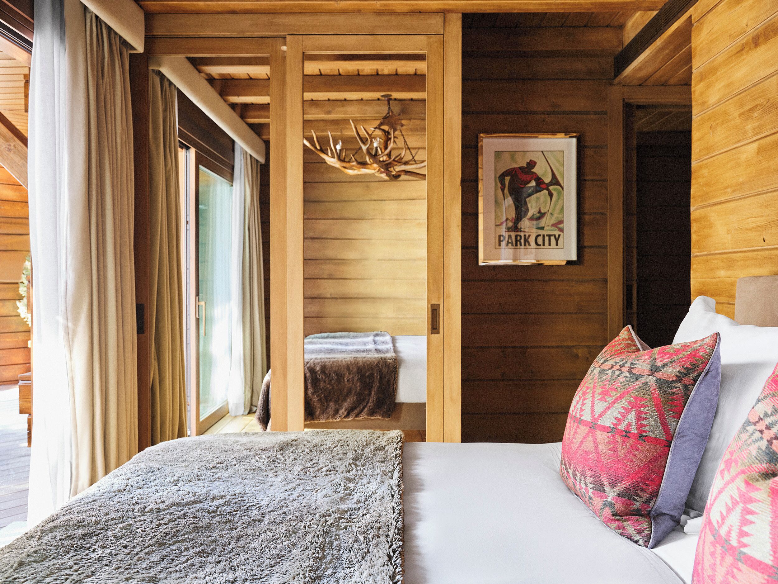 A wooden cabin room with a bed, a framed picture, and a deer antler chandelier.