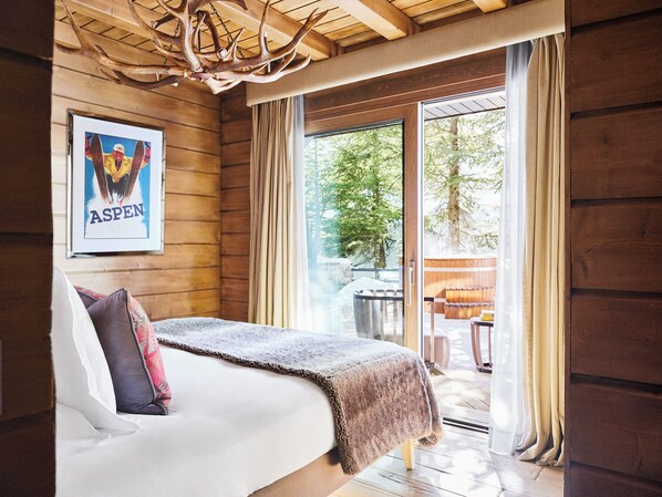A wooden cabin bedroom with a bed, a framed picture on the wall, and a large window with curtains.