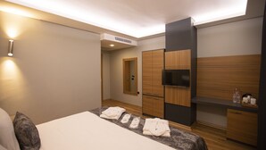 Une chambre d’hôtel moderne équipée d’un lit, d’un téléviseur à écran plat, d’armoires en bois et d’un système de climatisation intégré.
