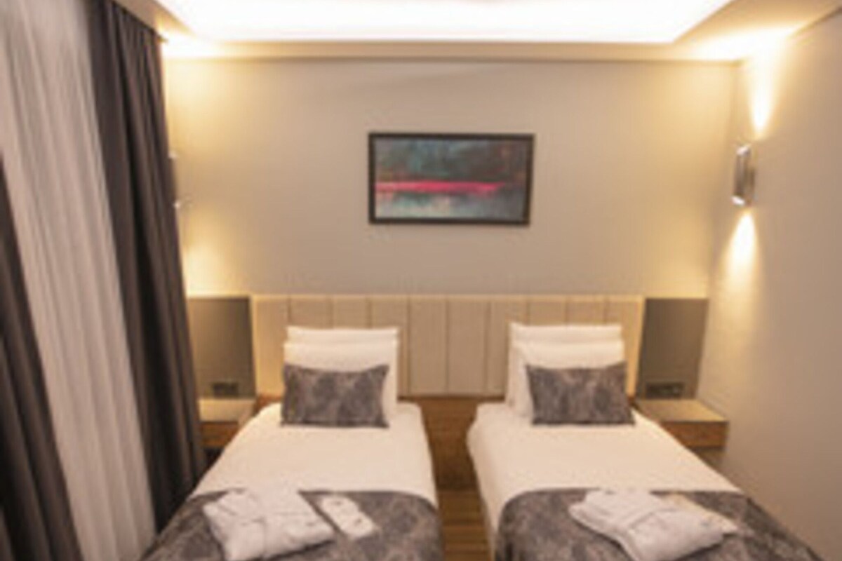 Quarto de hotel com duas camas, um quadro na parede e uma mesa de cabeceira com abajur.