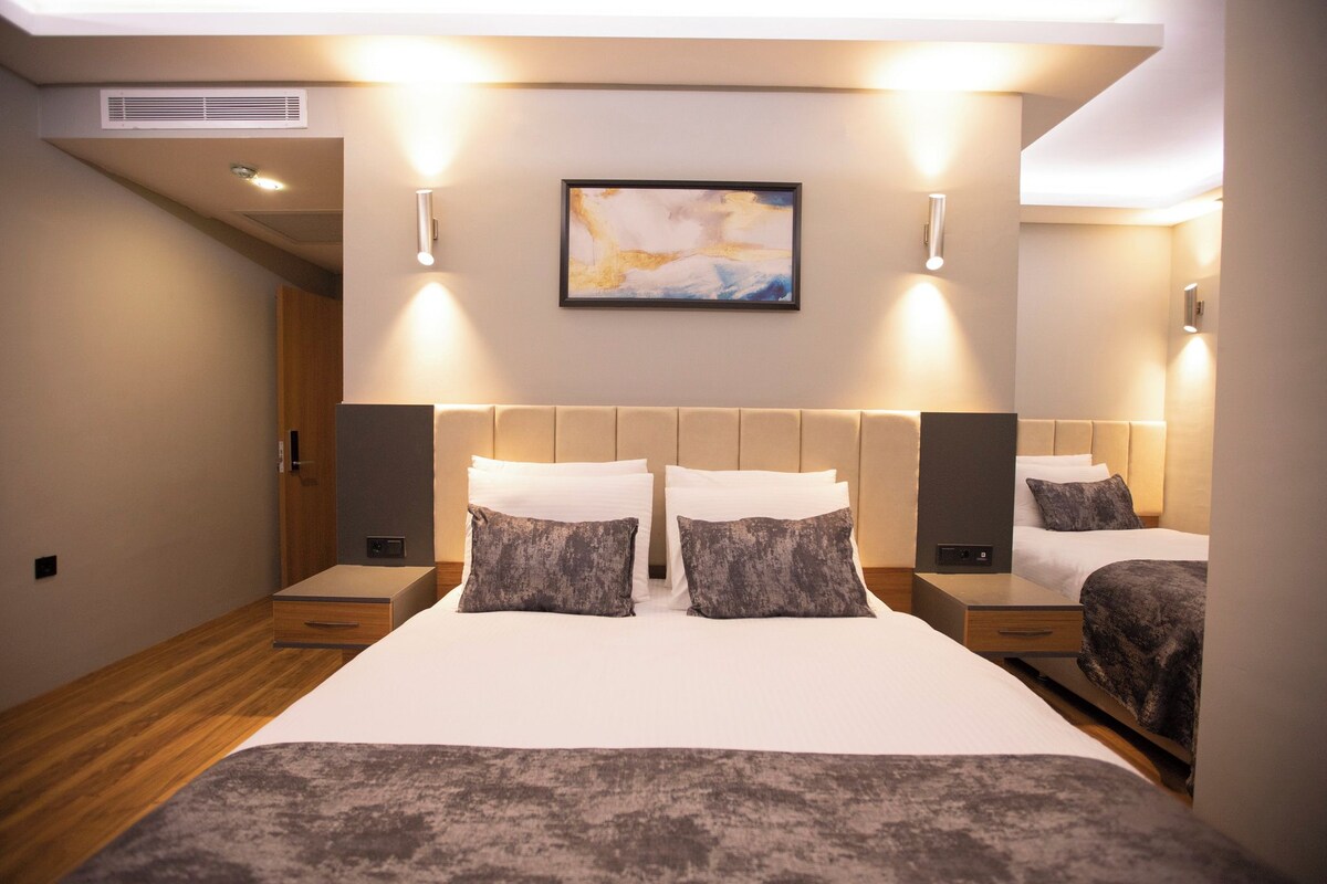 Una habitación de hotel moderna con una cama grande, mesitas de noche, cabecera y una obra de arte colgada en la pared.