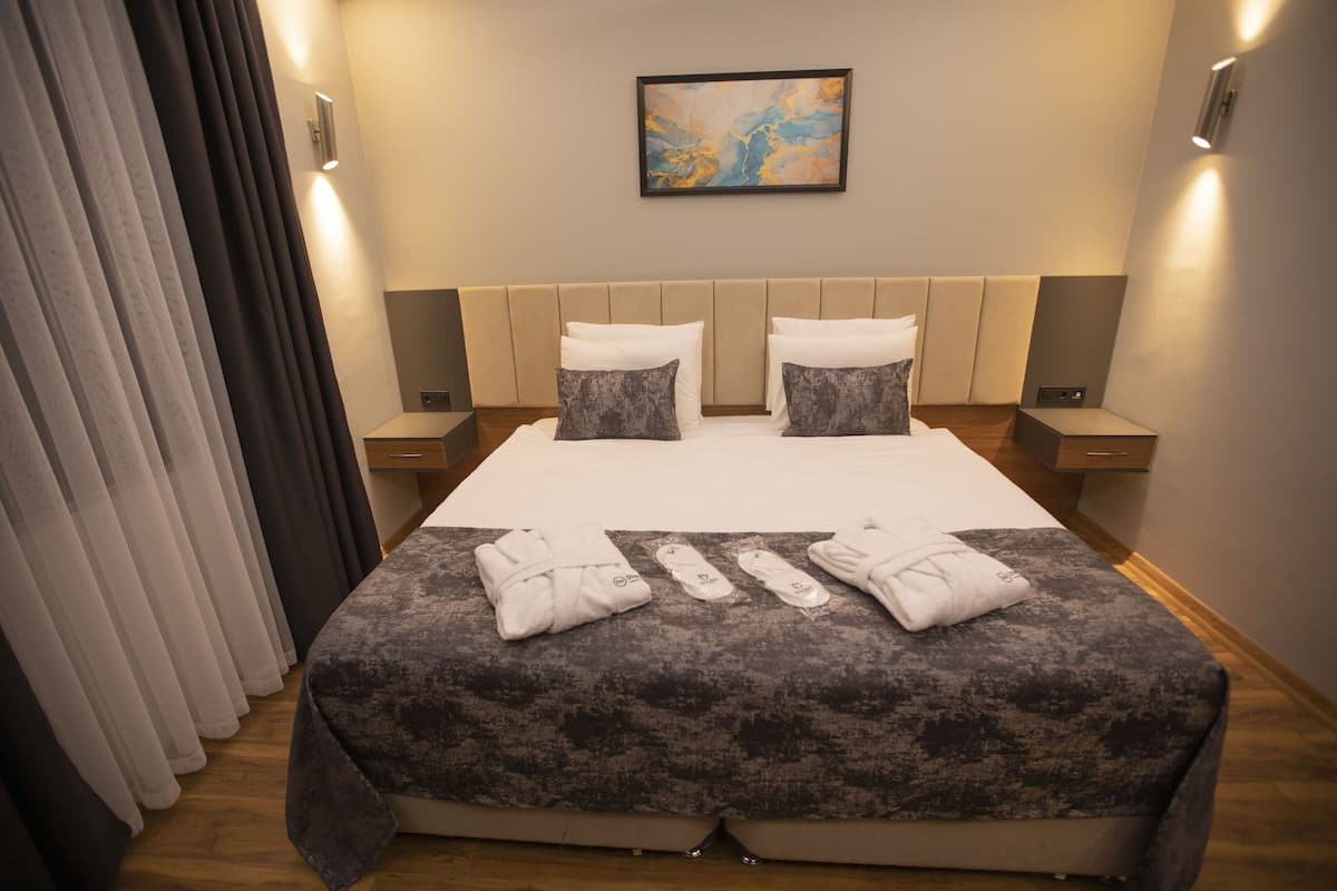 A hotel room with a large bed, two pillows, a headboard, bedside tables, and a painting on the wall.