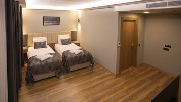 A hotel room with two beds, wooden flooring, a door, and a wall-mounted light fixture.