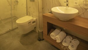 Une salle de bain moderne dotée d’une douche à parois de verre, de toilettes, d’un lavabo avec un plan de travail en marbre et d’un miroir avec éclairage intégré.