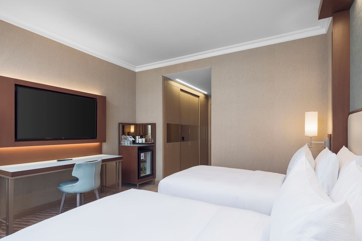 A hotel room with a bed, a desk, a chair, a television, and a minibar.