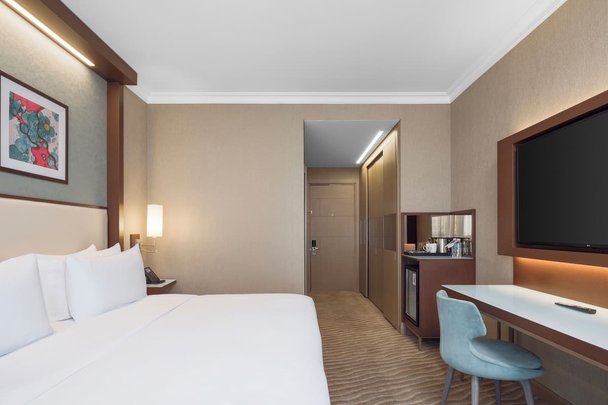 A hotel room with a large bed, a desk with a chair, a television, and a minibar.