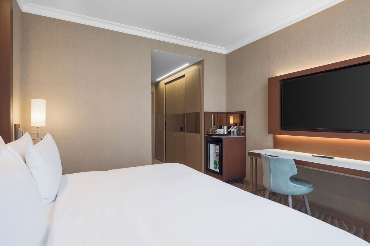 A hotel room with a bed, a desk, a chair, a TV, and a minibar.