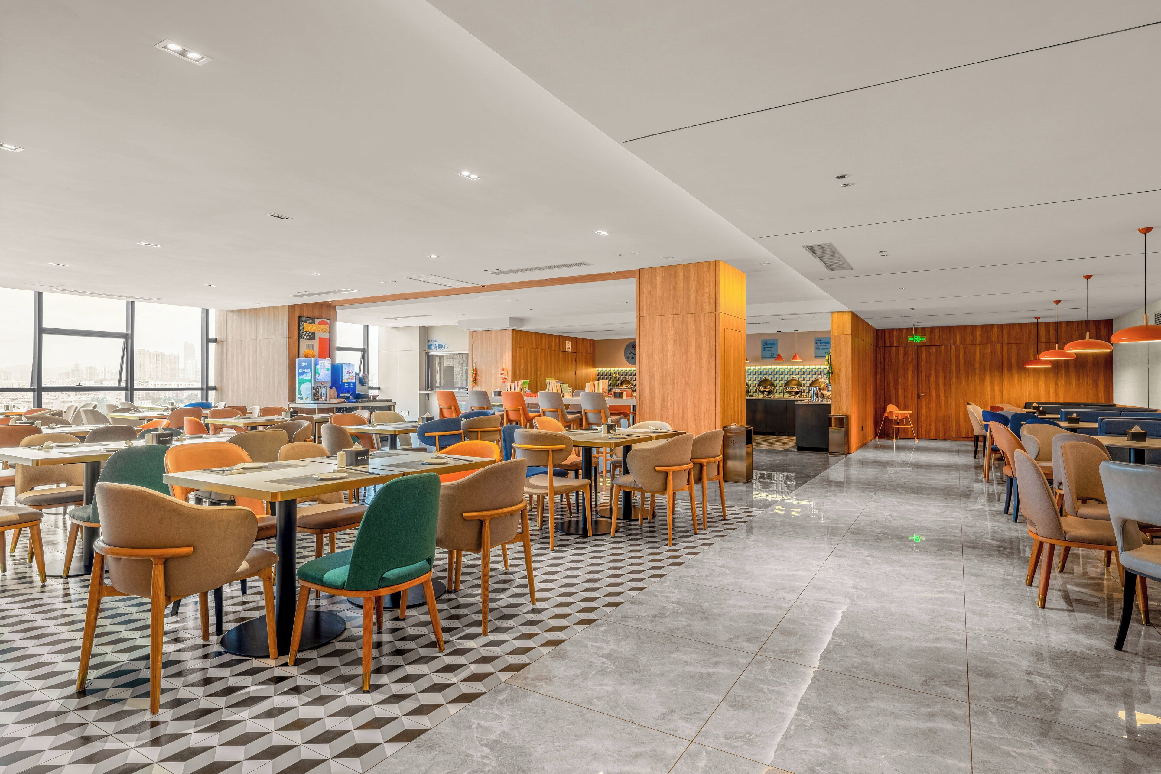 Un comedor moderno con varias mesas y sillas, un mostrador de recepción y vistas a la ciudad.