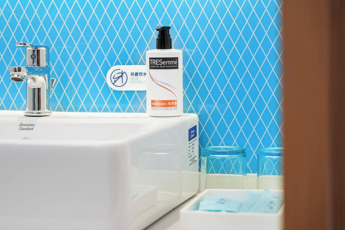 A bathroom with a white sink, a hand wash dispenser, and a glass container.