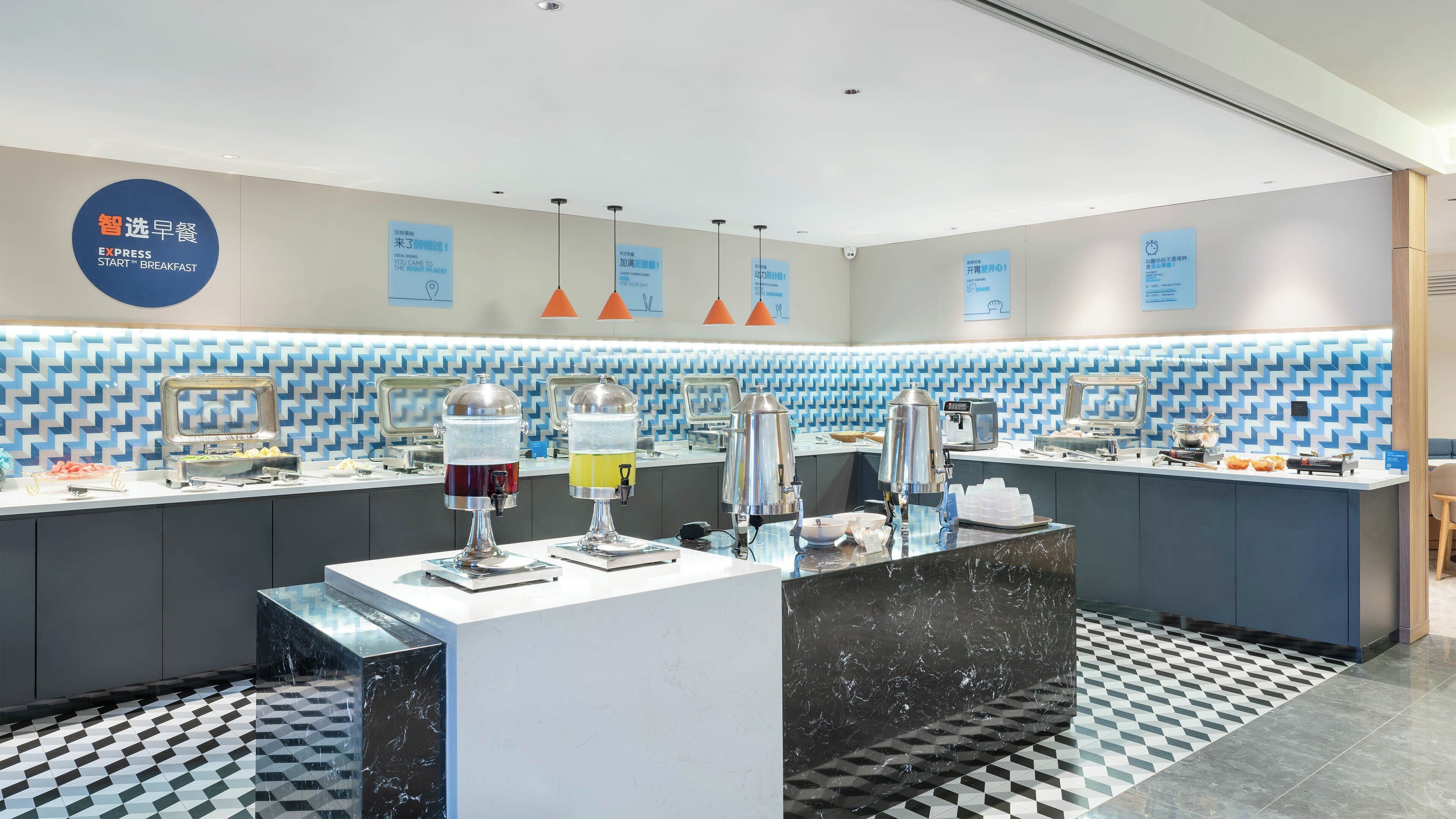 A breakfast area with self-service beverage dispensers, a buffet counter, and a clock on the wall.