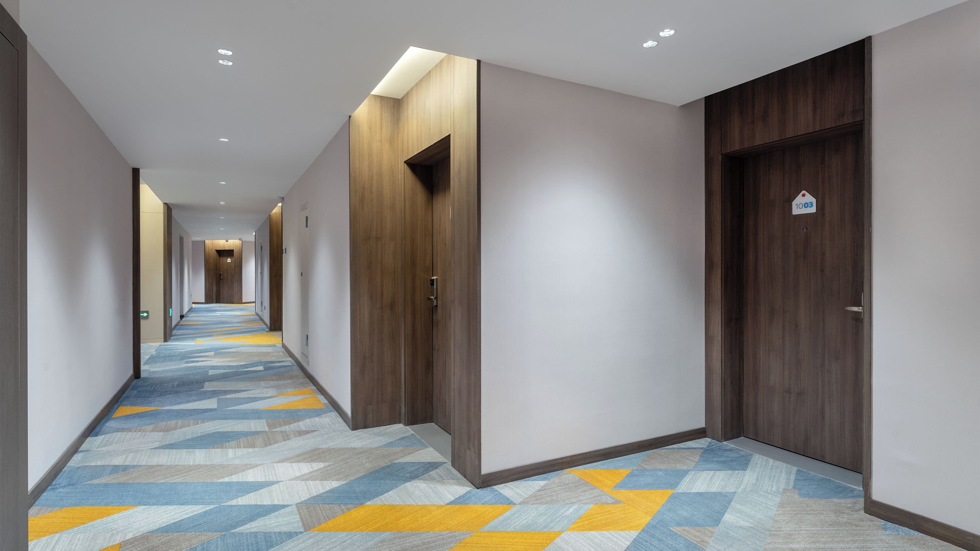 A hotel hallway with wooden doors, a patterned carpet, and recessed lighting.