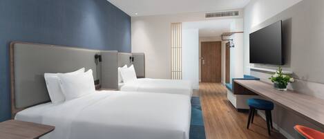 Habitación de hotel con dos camas, un escritorio, una silla, un televisor y una planta.