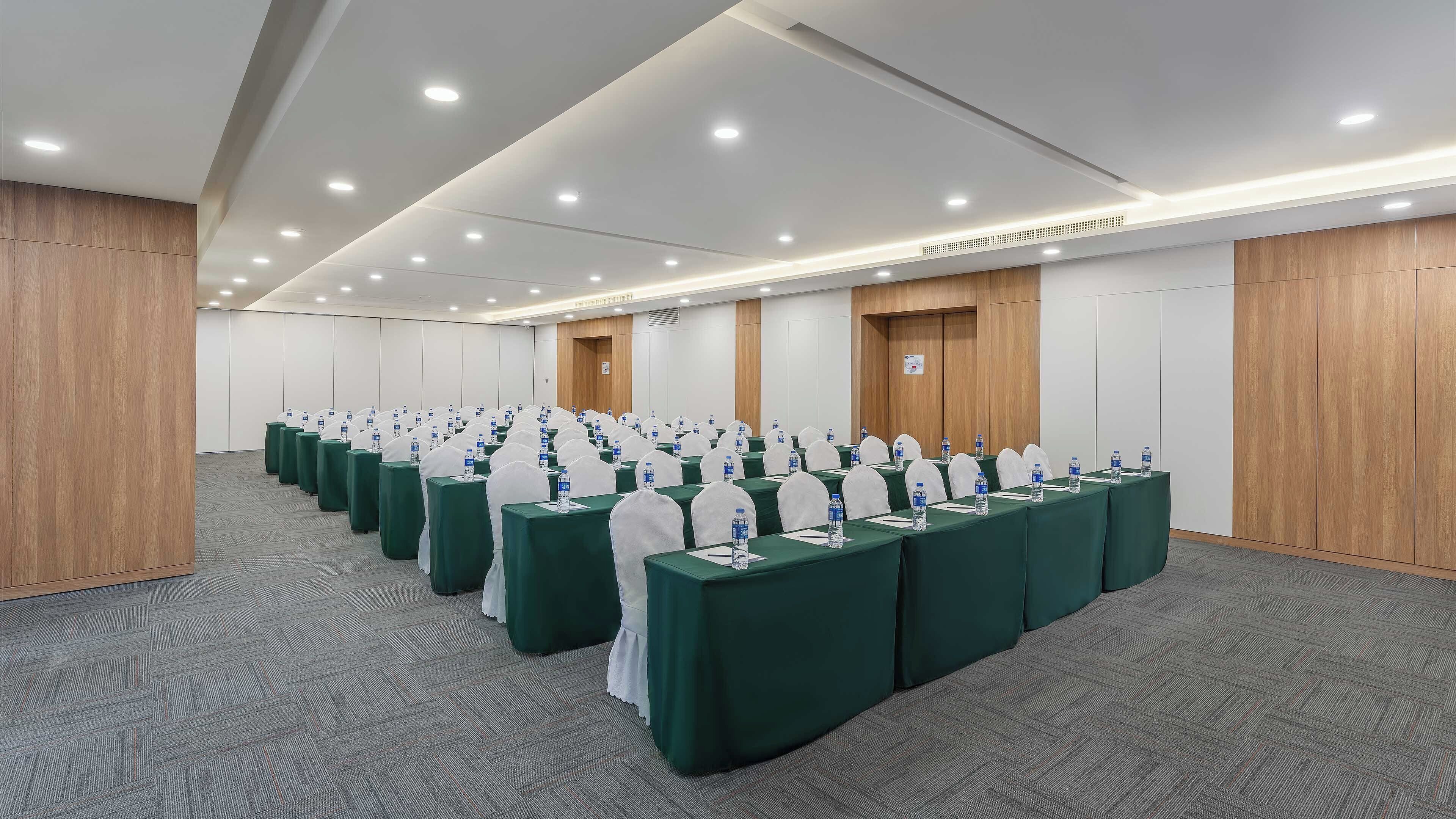Un salón de conferencias con filas de mesas, cada una con una botella de agua y una silla blanca.