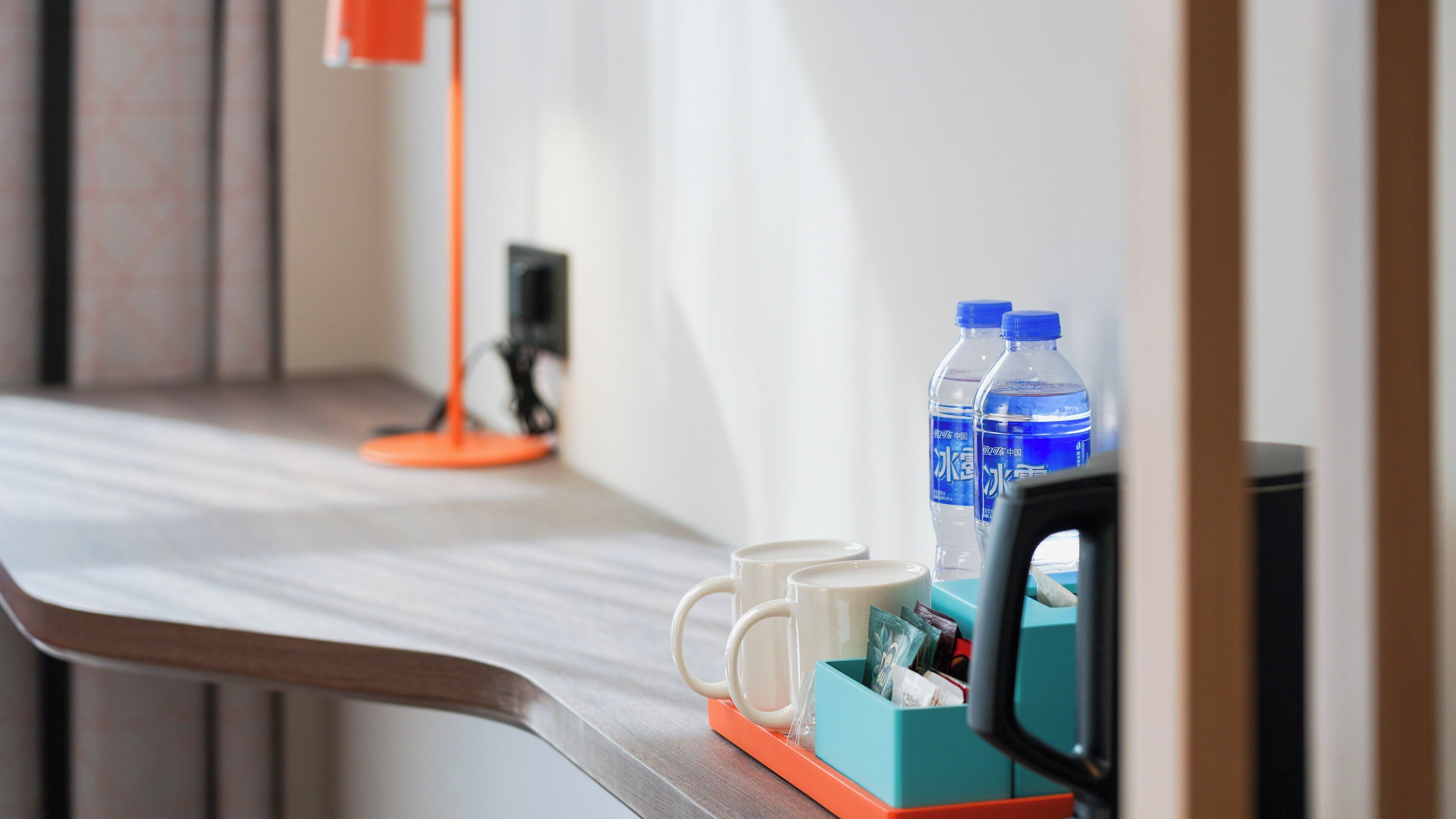 Habitación de hotel con un escritorio de madera, dos botellas de agua, una taza y una pequeña caja con artículos.