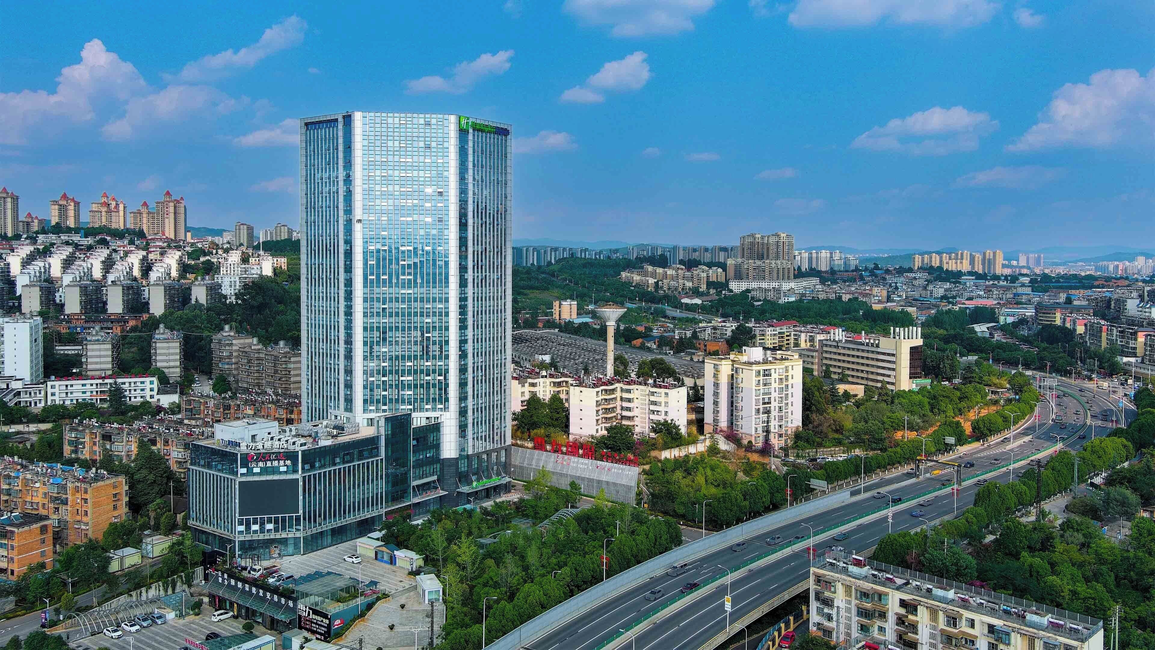 Un immeuble de grande hauteur doté d’une façade moderne en verre, entouré d’immeubles résidentiels de taille moyenne et bordé par une autoroute très fréquentée.