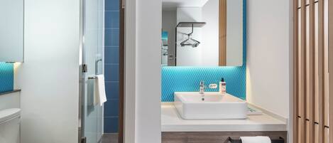 Un baño moderno con cabina de ducha de vidrio, un lavamanos blanco y un espejo con toallero.