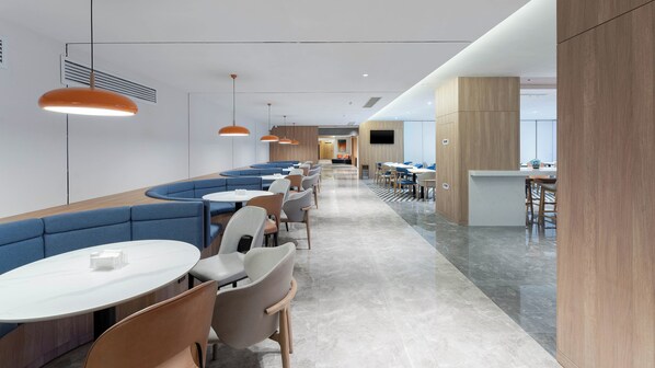 Un restaurant moderne avec des banquettes bleues, des tables rondes blanches et des luminaires suspendus orange.