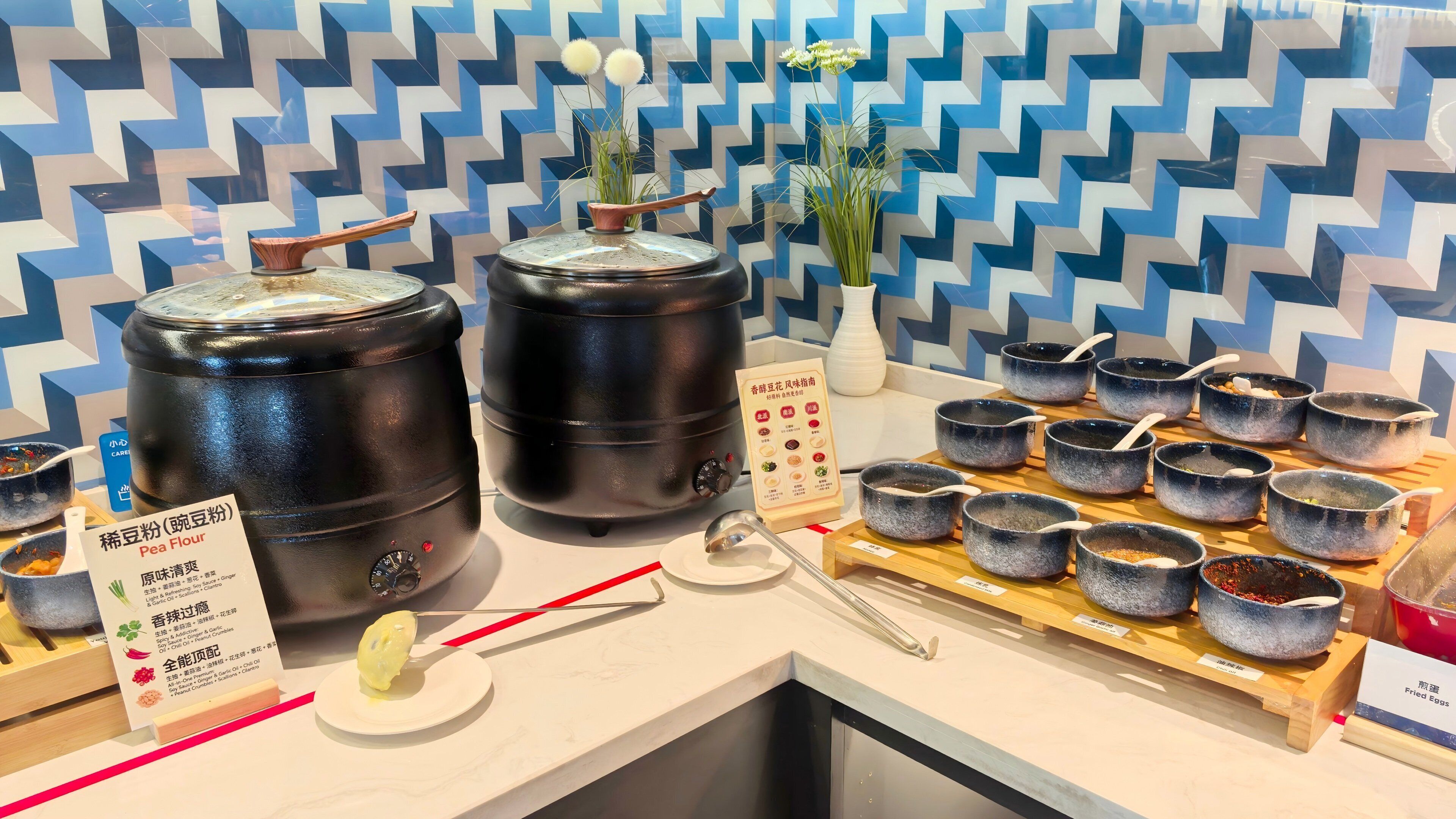 A buffet setup with large black containers, small bowls with spoons, and a menu stand.