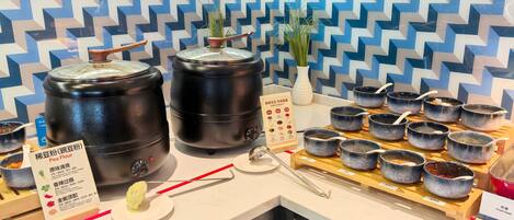 A buffet setup with large black containers, small bowls with spoons, and a menu stand.