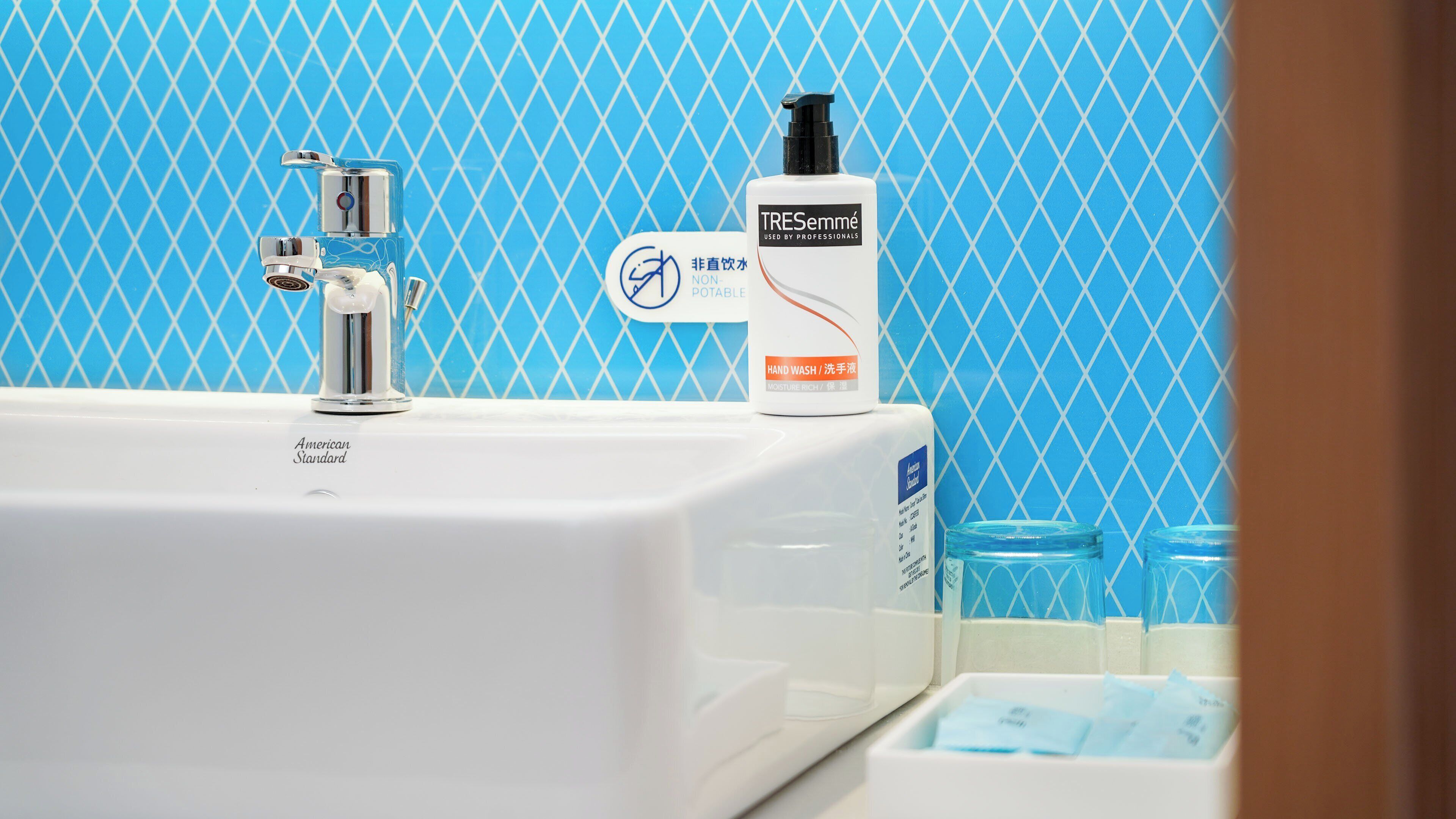 Un lavabo de salle de bain avec un robinet, un flacon de savon liquide pour les mains et un récipient en verre.