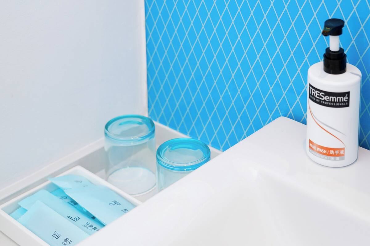 A bathroom with a white sink, a bottle of hand wash soap, and two blue glass containers.