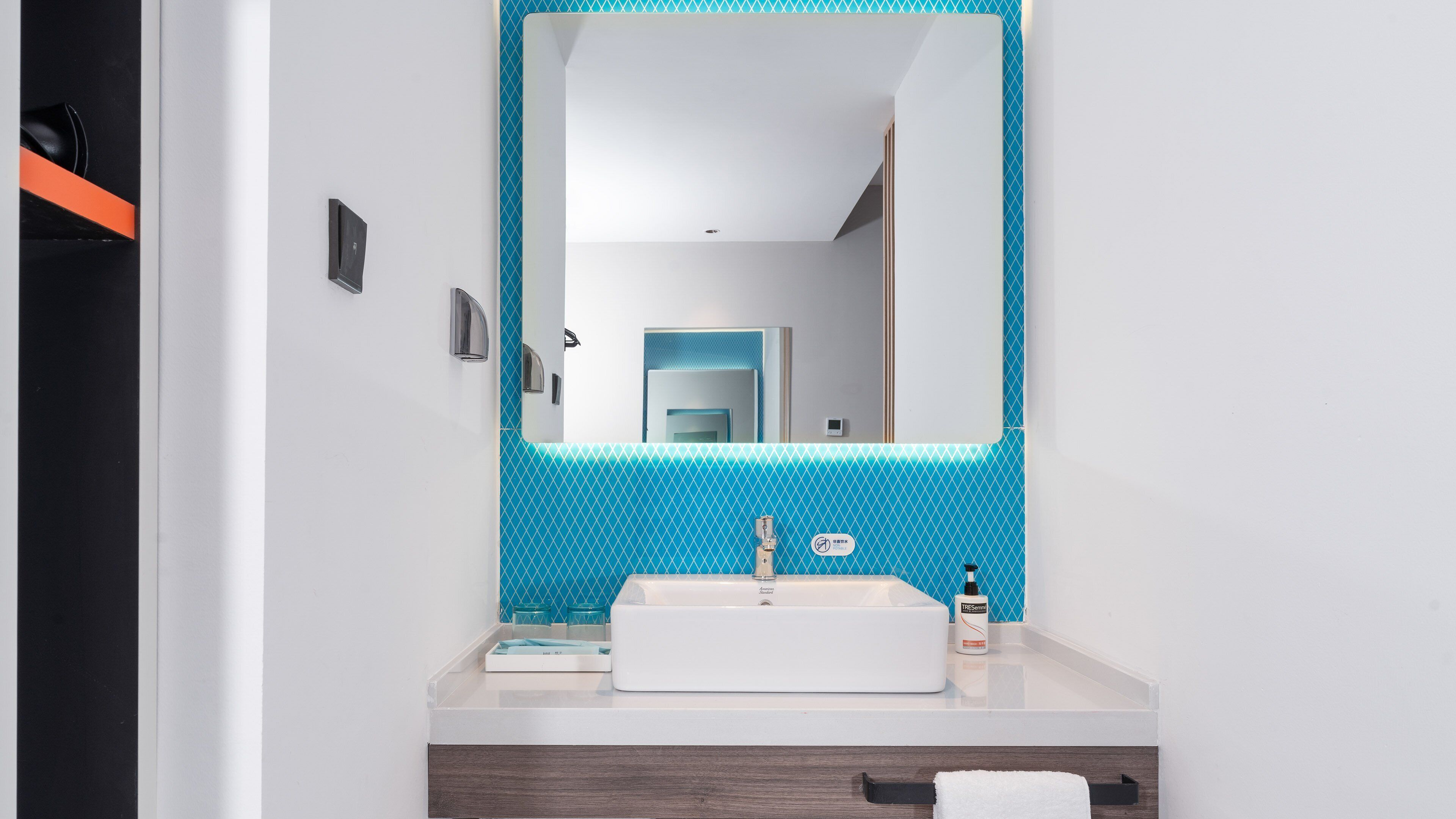 Un baño moderno con un lavabo blanco, un espejo y un salpicadero de azulejos azules estampados.