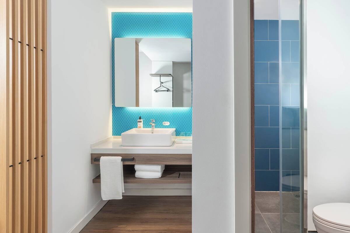 A modern bathroom with a wooden panel wall, a white sink with a blue backsplash, and a glass shower enclosure.