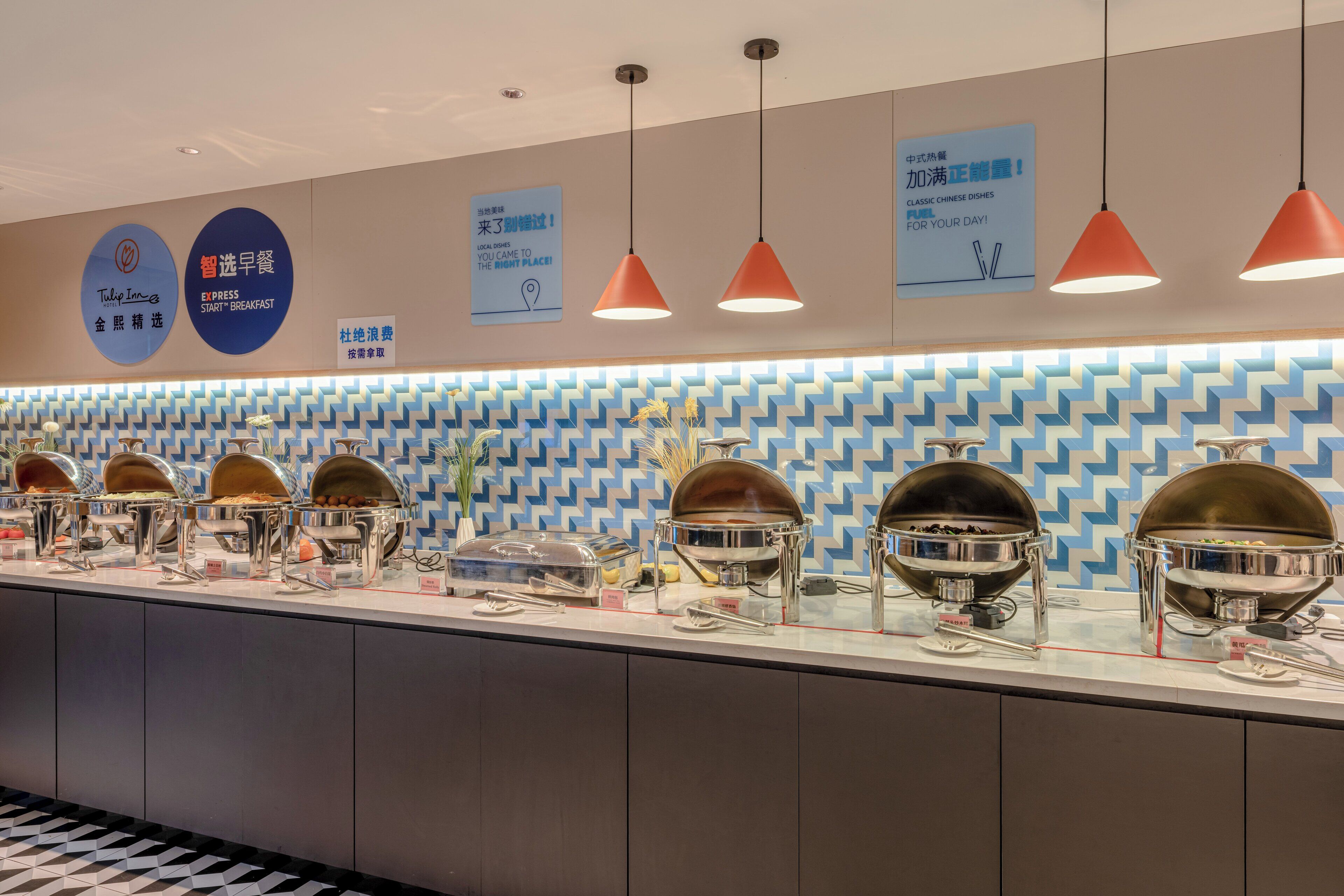 A buffet area with multiple food stations, overhead lighting, and a patterned wall in the background.