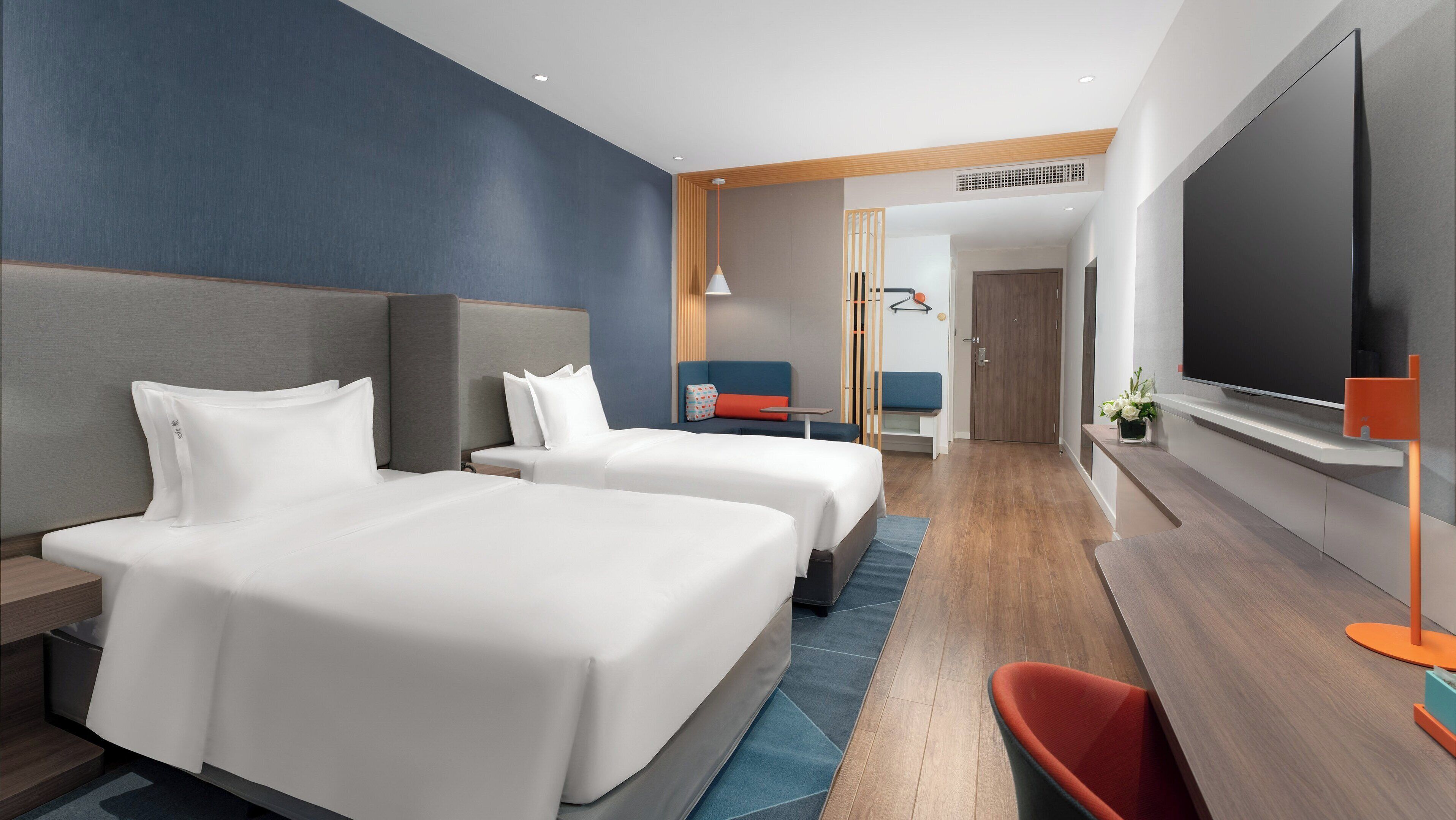 A hotel room with two beds, a TV, a desk, and a seating area.