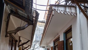 A narrow alleyway with buildings on either side, featuring wooden doors and a tiled floor.