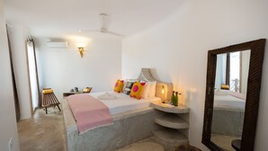 A bedroom with a bed, bedside tables, a mirror, and a bathroom with a sink and mirror.
