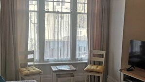 Quarto com janela, duas cadeiras, uma mesinha e uma televisão.