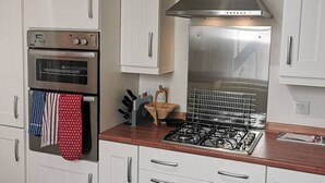 Une cuisine avec des armoires blanches, une hotte de cuisinière en acier inoxydable, un four double et une cuisinière à gaz.