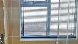 Une salle de bain comprenant un lavabo, une douche en verre, une fenêtre avec des stores et un porte-serviettes.