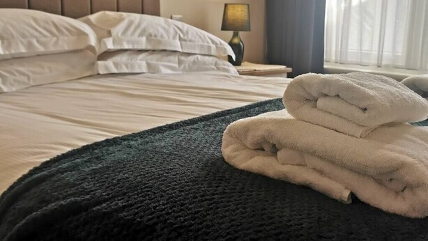 Un lit bien fait, avec des draps blancs et une serviette pliée posée sur une couverture vert foncé.