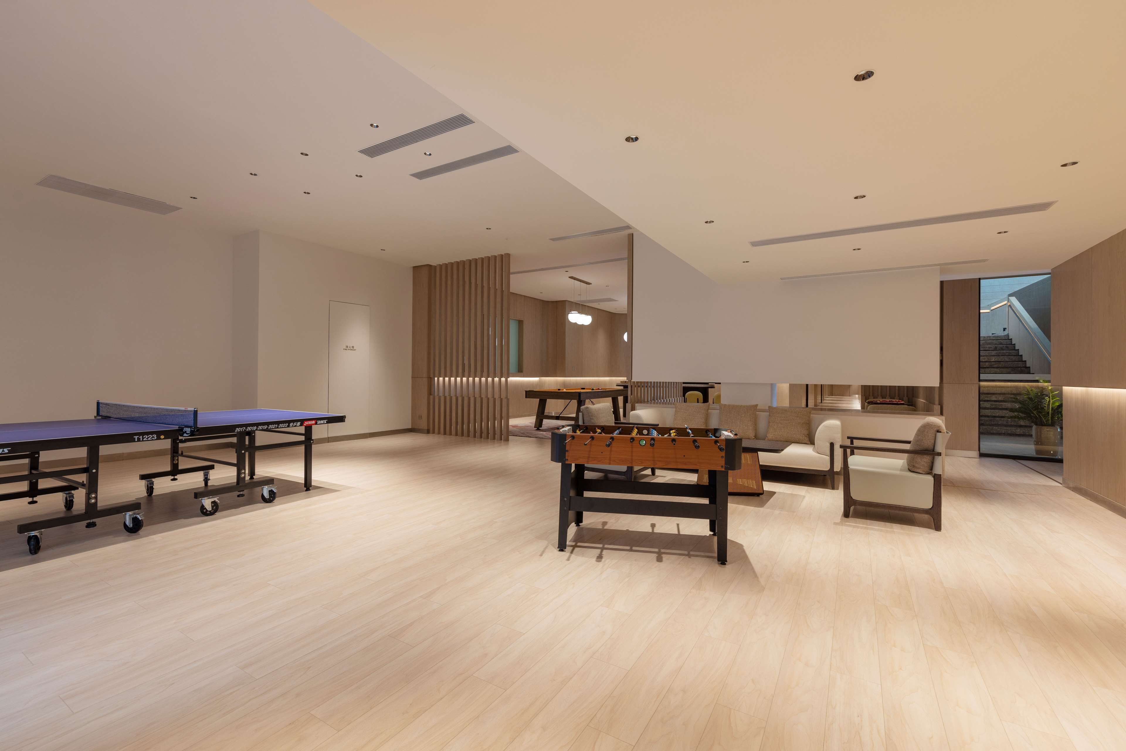 A modern indoor space with ping pong tables, a foosball table, and a sofa area.