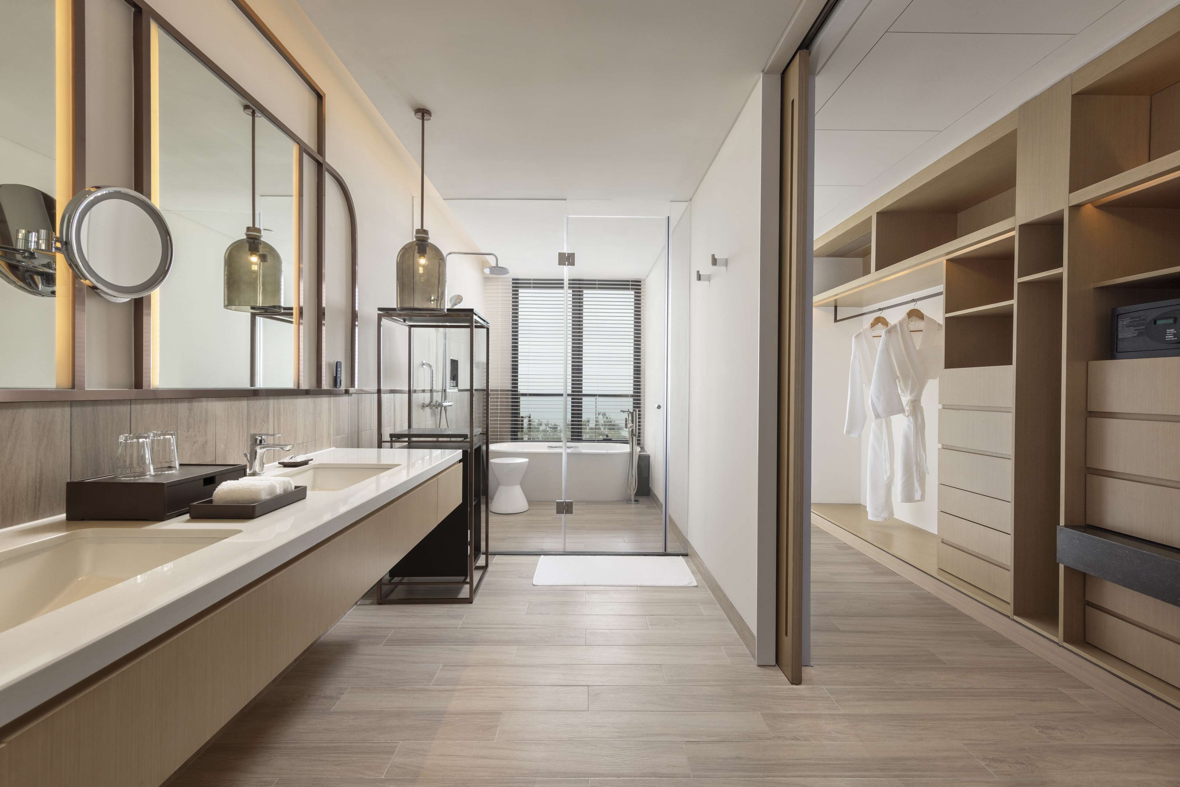 A modern bathroom with a large mirror, a sink, a toilet, and a shower area. There is a walk-in closet with shelves and a hanging rack.