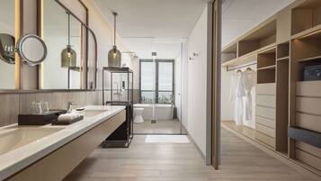 A modern bathroom with a large mirror, a sink, a toilet, and a shower area. There is a walk-in closet with shelves and a hanging rack.