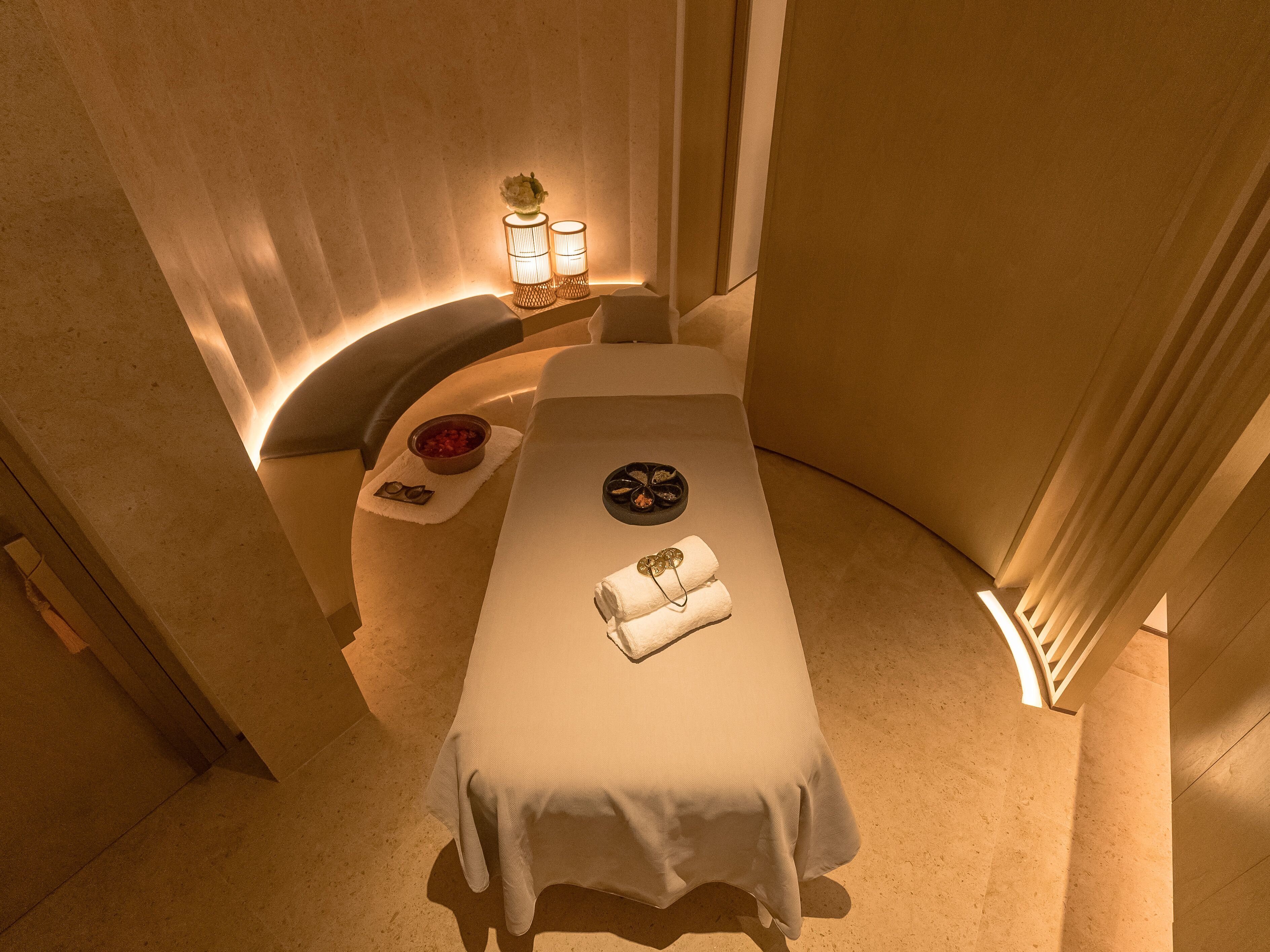 A spa room with a massage table, a small table with a bowl of fruit, and two wall-mounted lamps.
