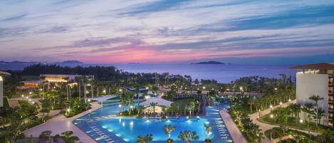 Relax by the infinity pool surrounded by lush greenery and palm trees, with a scenic view of the nearby water.