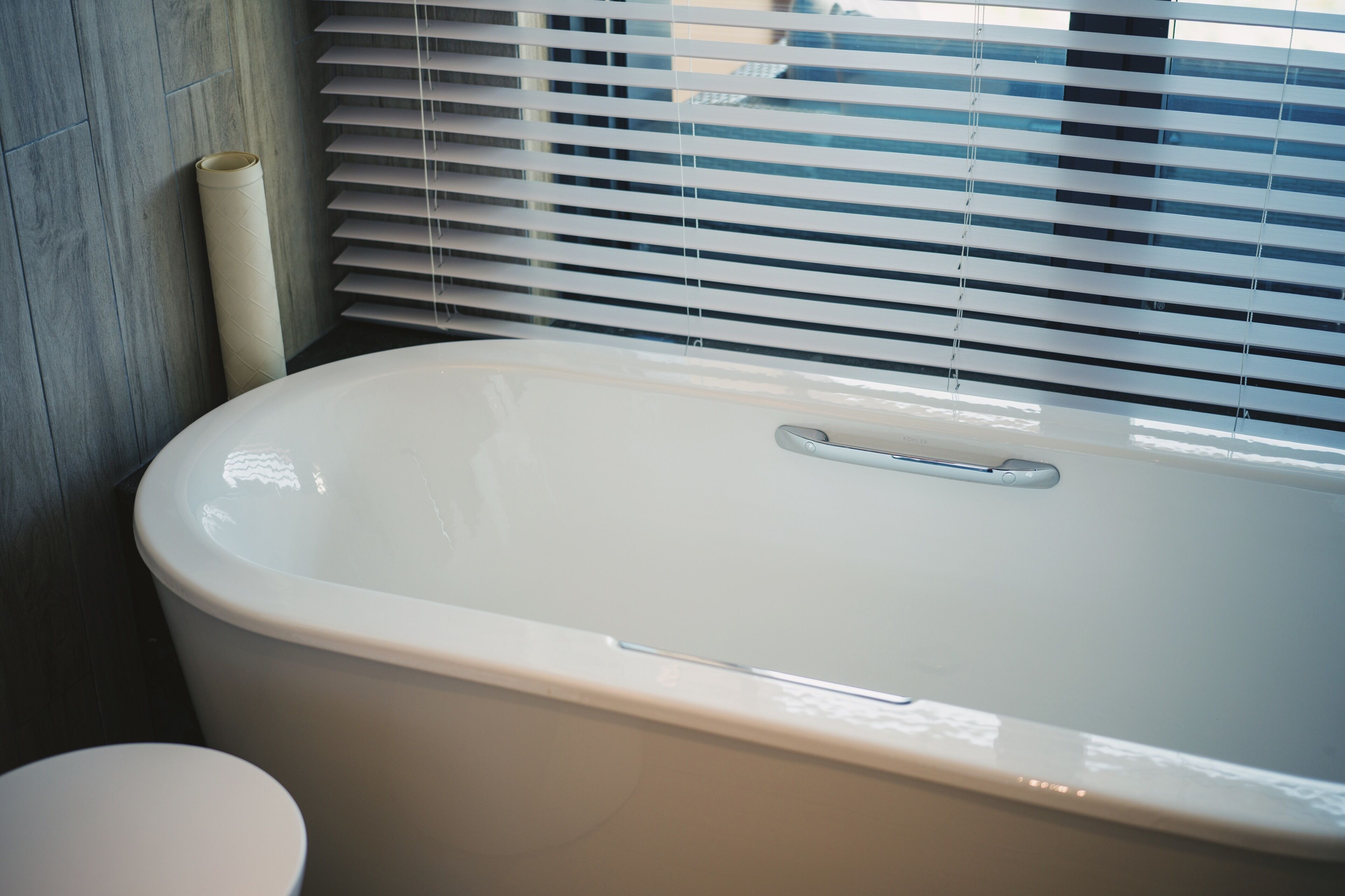 Un baño con bañera, inodoro y ventana con persianas.